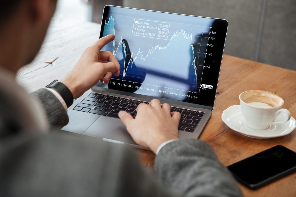 Homem observando gráfico de investimentos em notebook. 
Homem fazendo trade em notebook enquanto toma um café.